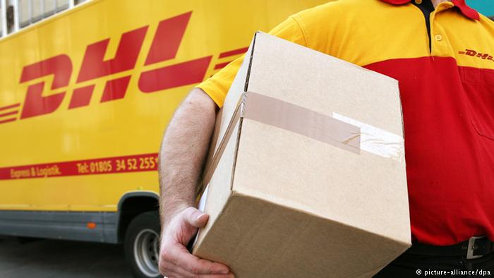 Сотрудник DHL несет пакет на фоне машины с логотипом компании