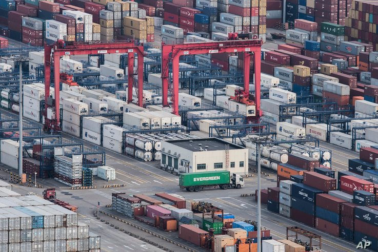 ФАЙЛ - Грузовой грузовик проезжает среди штабелированных грузовых контейнеров в порту Яншань в Шанхае, Китай, 29 марта 2018 года.