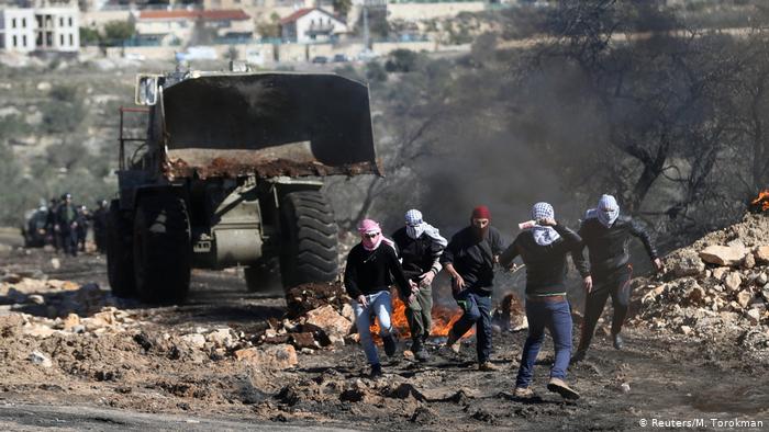 Молодые палестинцы в масках убегают от бульдозера в дыму горящего мусора